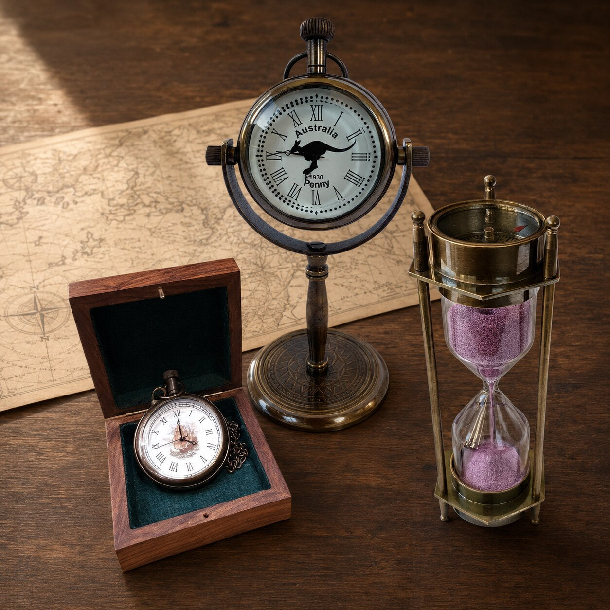 Australian Penny stand clock, boxed pocket watch and purple-sand hourglass displayed on a walnut desk with a vintage map