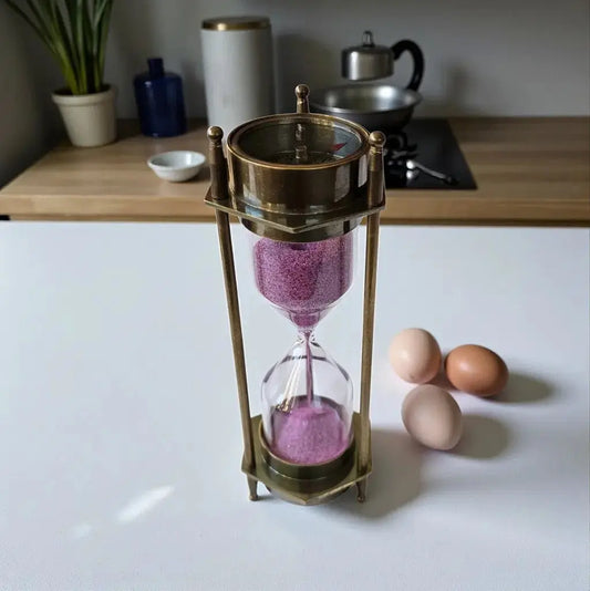 Hourglass with pink sand on a kitchen counter next to three eggs