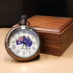 A vintage-inspired pocket watch with the Australian flag design on the cover, displayed on a wooden box.