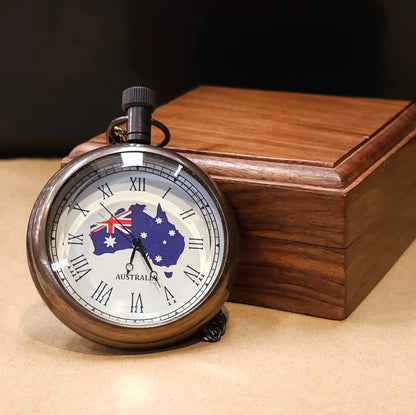 A vintage-inspired pocket watch with the Australian flag design on the cover, displayed on a wooden box.
