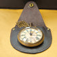 A vintage pocket watch with a brass body displayed in an open wooden box with a blue velvet interior.